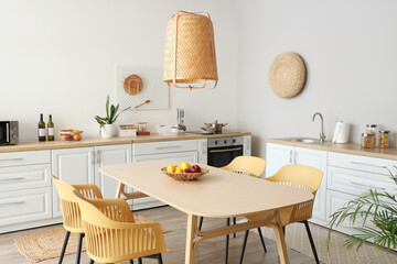 Interior of stylish kitchen with dining table, chairs, white counters and lamp
