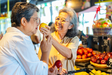 Happy Asian senior woman shopping buying food and grocery at supermarket. Elderly women friends enjoy healthy lifestyle choosing and buying organic fresh food, vegetable and fruit at shopping mall.