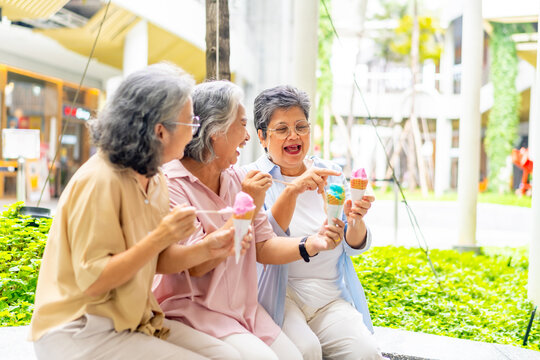 Group of Happy Asian senior woman friends eating ice cream together at shopping mall. Healthy elderly woman enjoy and fun outdoor lifestyle travel and shopping in the city on summer holiday vacation.