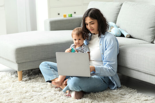 Cute baby and happy young mother working with laptop on maternity leave at home