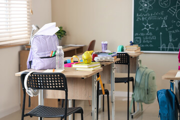 Apple with eyeglasses, books and backpack on desk in classroom