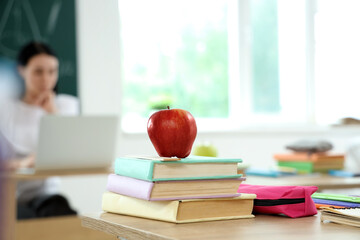 Apple with books and pencil case on desk in classroom, closeup