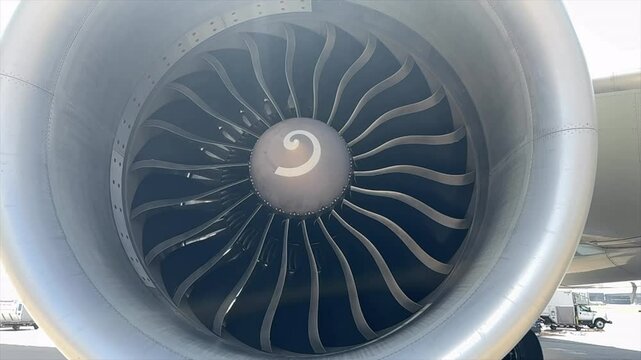 Close-up view of a commercial aircraft jet engine with fan blades windmilling in the breeze while the airplane is parked on the ground.