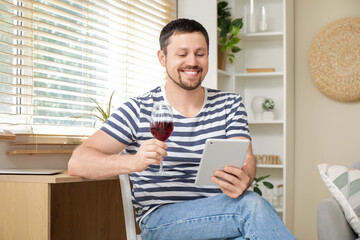 Handsome man with wine and tablet computer having online date at home