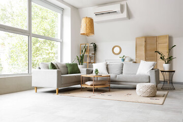 Interior of light living room with mirror, grey sofas and folding screen