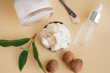 Jars of shea butter with nuts and cosmetic dropper bottle on beige background