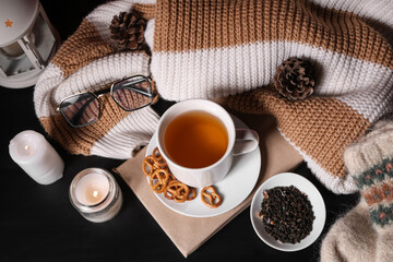 Beautiful composition with book, cup of tea, winter decorations and warm clothes on black background