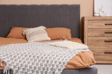 Big comfortable bed with pillows and chest of drawers in interior of bedroom