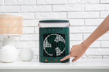 Woman turning portable table fan on shelf at home