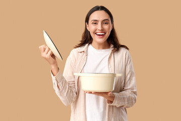 Young woman holding cooking pot with tasty soup on beige background