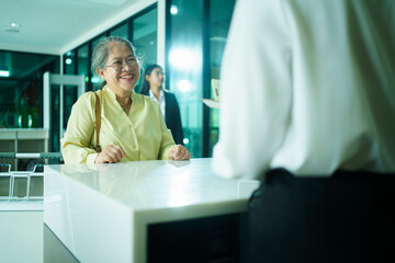 Elderly Asian female woman is proceeding baggage check-in at airline checkin counter in modern...