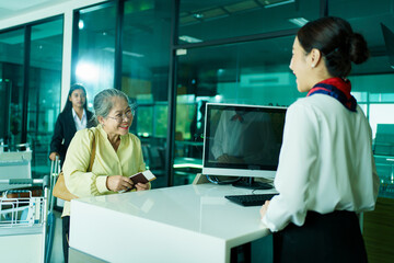 Fototapeta premium Elderly Asian female woman is proceeding baggage check-in at airline checkin counter in modern airport.
