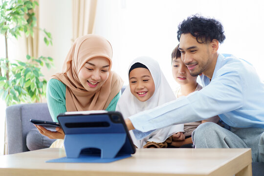 Asian muslim family enjoy watching a funny contents on a tablet while sit together in cozy living room.