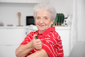 Diabetic senior woman using lancet pen in kitchen