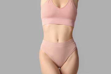 Beautiful young woman in pink underwear on grey background, closeup