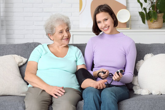 Young nurse with senior woman measuring blood pressure on sofa at home