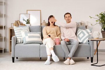 Obraz premium Young man covering his girlfriend's eyes while watching TV on sofa at home