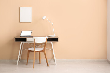Table with laptop and empty poster on beige wall