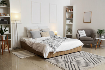 Interior of stylish lamp bedroom with cozy bed, grey armchair and glowing lamps