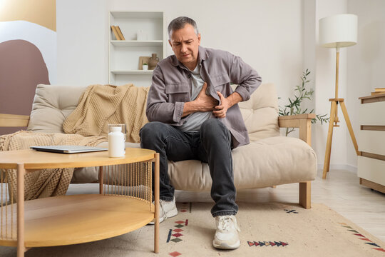 Mature man suffering from chest pain on sofa at home