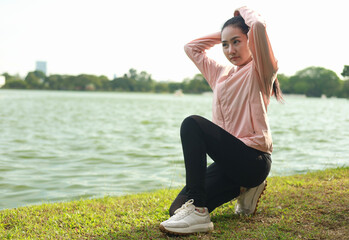 A young woman is preparing to exercise in a park on a sunny day, arranging her body.