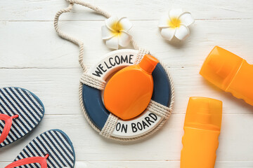 Composition with flip-flops, decorative lifebuoy ring, plumeria flowers and bottles of sunscreen cream on white wooden background
