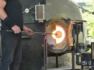 Skilled glassblower manipulating glowing molten glass, blowing and forming intricate art using traditional workshop techniques and specialized tools