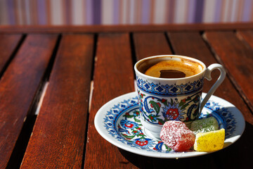 Turkish coffee in traditional ornate cup on wooden table with colorful Turkish delight in sunny day...