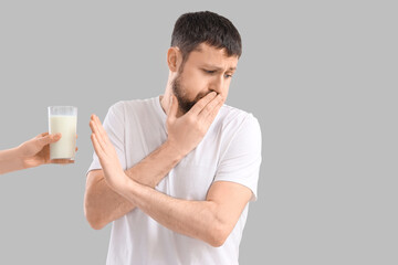 Sick young man rejecting female hand with glass of milk on light background. Food Allergy Awareness...