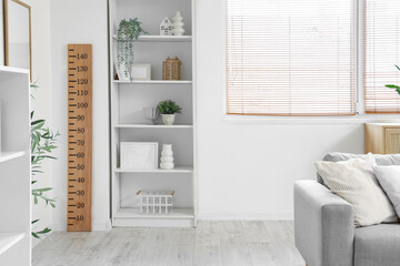 Interior of modern living room with sofa, shelving units and wooden stadiometer near window