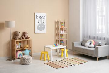 Interior of children's room with sofa, lamp, many toys in shelving units and play table near beige wall