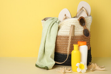 Wicker bag, bottles of sunscreen cream, flower and beach accessories on yellow background, closeup