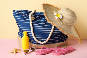 Striped bag, bottle of sunscreen cream and beach accessories on color background, closeup