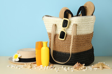 Wicker bag, bottles of sunscreen cream, stones and beach accessories on color background, closeup