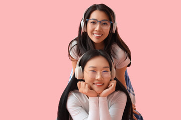 Beautiful young happy Asian sisters in headphones on pink background