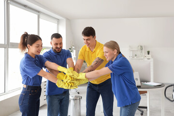 Team of young janitors putting hands together in office