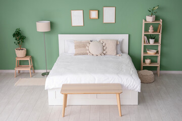 Interior of stylish room with bed, shelf unit and blank frames
