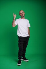 Fototapeta premium Young man with a variety of emotions, wearing a white t-shirt standing against a green background. Studio shot with copy space.
