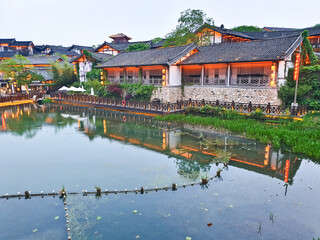 Fototapeta premium A tranquil canal scene at dusk with traditional Chinese buildings, soft lights reflecting in water, surrounded by nature and architecture 