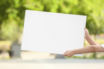 Female hands holding blank poster on city street