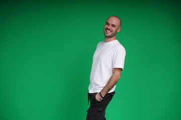 Fototapeta premium Young man with a variety of emotions, wearing a white t-shirt standing against a green background. Studio shot with copy space.
