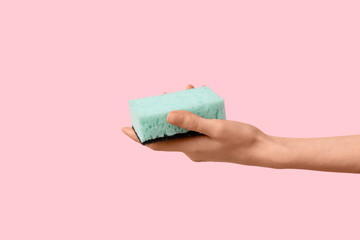 Hand holding sponge for cleaning on pink background