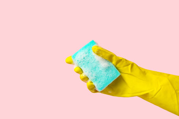 Hand in rubber glove holding sponge for cleaning on pink background