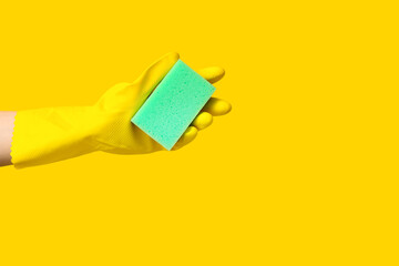 Hand in rubber glove holding sponge for cleaning on yellow background