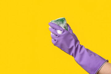 Hand in rubber glove holding sponge for cleaning on yellow background
