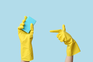 Hands in rubber gloves holding sponge for cleaning on blue background