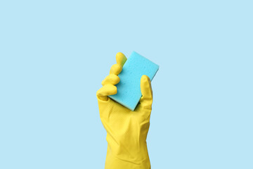 Hand in rubber glove holding sponge for cleaning on blue background