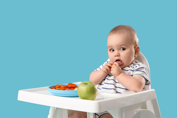 Cute little baby eating vegetables in high chair on blue background