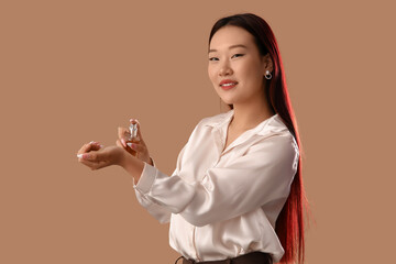 Beautiful Asian woman applying perfume on beige background