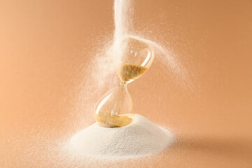 Crystal hourglass and pouring sand on beige background